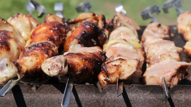 Chicken and pork grilled on charcoal in a barbecue. Meat rotates and has golden skin. moving the camera. Close up