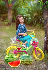 Girl sitting on the grass next to the watermelons and bright beautiful bike