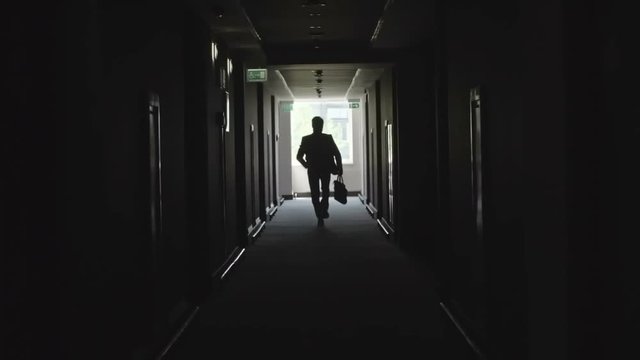 Unrecognizable businessman checking time on wristwatch while running with briefcase through dark corridor towards the camera 