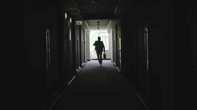 Unrecognizable businessman running with briefcase through dark corridor towards the camera in slow motion