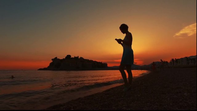 woman using smartphone at sunset beach of island  Sveti Stefan, Montenegro