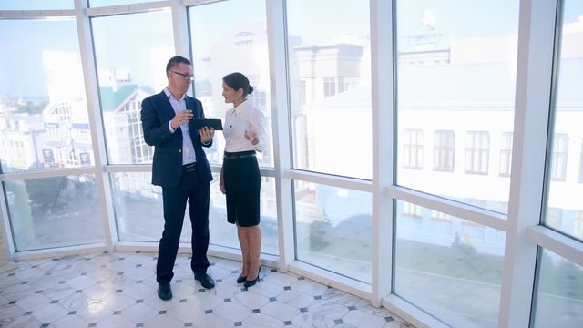 Business, architecture and office concept. Two successful businessmen discuss project on tablet in clean bright office mear panoramic window. HD.