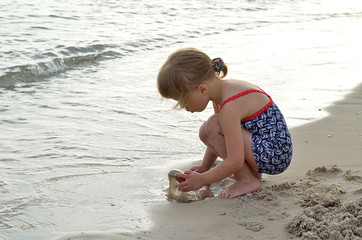 Sweet girl playing with sand on the seashore.