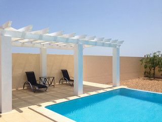 White poolside pergola, gazebo providing shade on a terrace patio area next to a swimming pool. Mobilestock. - obrazy, fototapety, plakaty