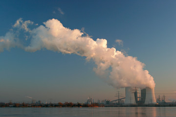 Coal Power Plant on a frozen Lake Smoking and Steaming against Blue Sky