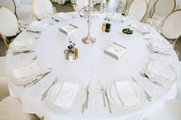 Elegant wedding reception white table arrangement restaurant, 
candlestick on table. Plates, forks and glasses