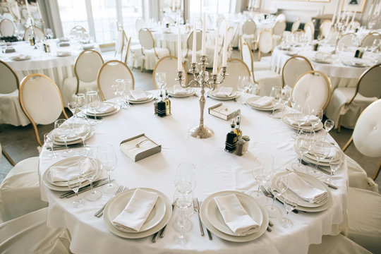 Elegant wedding reception white table arrangement restaurant, 
candlestick on table. Plates, forks and glasses