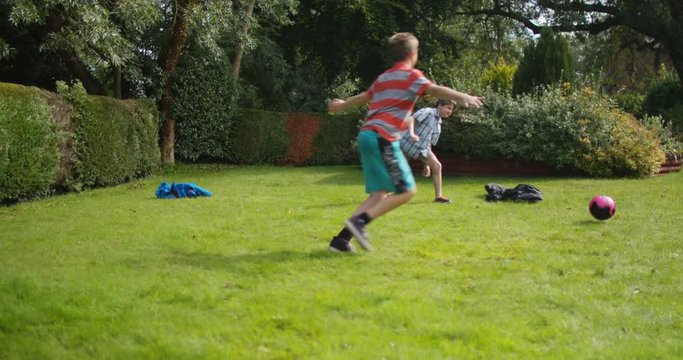  2 Active young boys playing soccer together in the garden. 