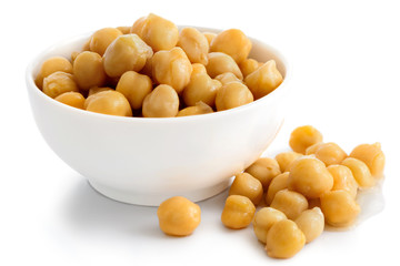 Cooked chickpeas in white bowl on white. Spilled chickpeas.