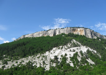 Fototapeta na wymiar scenic white rock with green forested slopes on blue sky background, closeup, Crimea 