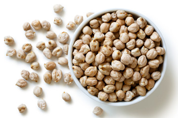 Dried chickpeas in white bowl on white from above. Spilled chickpeas.