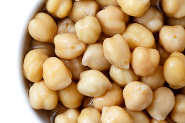 Detail of cooked chickpeas in white bowl on white from above.