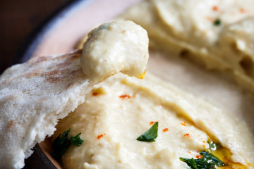 Detail of hummus on pita bread. Plate of eaten hummus in background.