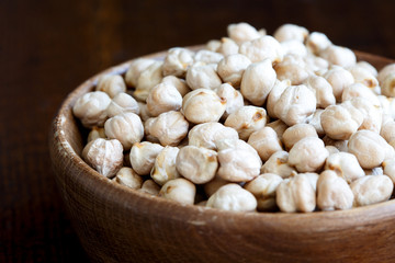 Detail of dried chickpeas in brown wooden bowl on dark.