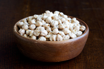 Dried chickpeas in brown wooden bowl isolated on dark.