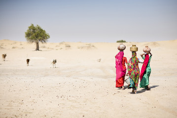 Women carrying water in traditional jugs in desert