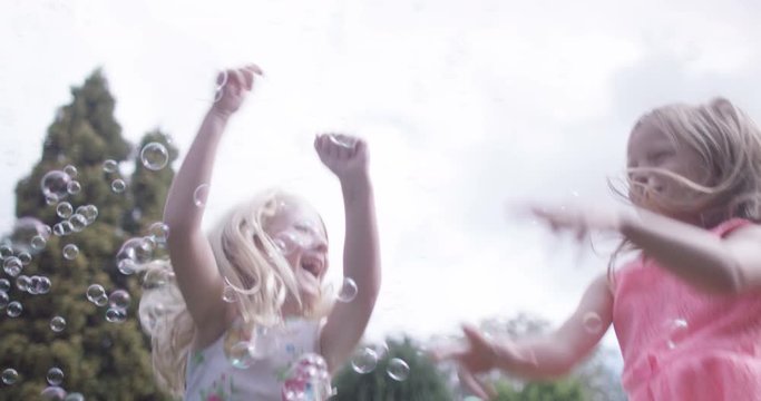  2 little girls having fun playing with bubbles in the garden. 