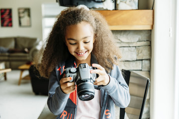 Smiling girl holding camera while sitting on chair