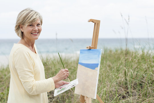 Older Caucasian woman painting beach outdoors