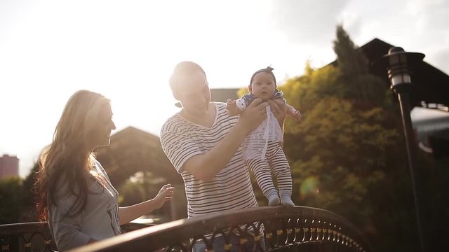 Young parents with a baby on the bridge in the park at sunset