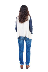 Fototapeta premium back view of standing young beautiful woman. girl watching. Rear view people collection. backside view of person. Long-haired girl with curly hair standing with his hands in his pockets. 