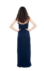 back view of standing young beautiful  woman.  girl  watching. Rear view people collection.  backside view of person. The dark curly girl in blue evening dress standing with hands on hips.  