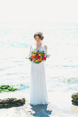 Fototapeta na wymiar Young bride holding wedding bouquet at the seashore