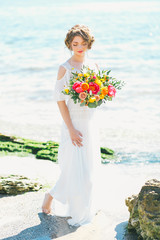 Fototapeta na wymiar Young bride holding wedding bouquet by the sea