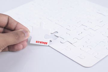 Closeup of businesspeople about to put four puzzle pieces with strategy word