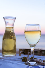 The carafe of white wine and a glass of wine on the beach, sunset, dinner by the sea, holiday, romance. Holidays in Greek wine in Greece.