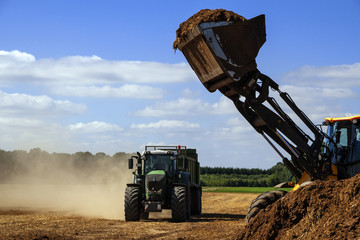 excavator with a shovel full of  organic fertilizer ready to fill the trailer of a tractor