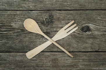 Crossed wooden fork and spoon on rustic wooden background, top view