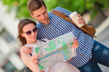 Happy tourist couple traveling in Europe smiling happy. Caucasian friends with city map in search of attractions. Young man with hot coffee and beautiful woman with big map
