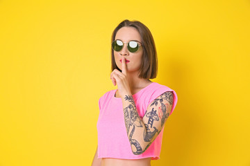 Beautiful young woman with tattoo wearing sunglasses and posing on yellow background