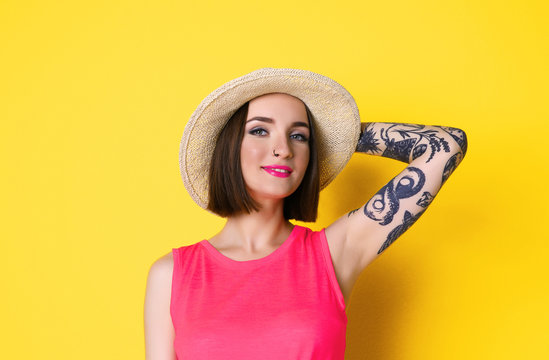 Beautiful young woman with tattoo wearing hat and posing on yellow background