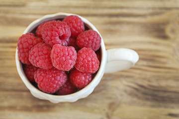 Fresh raspberry in cup on wooden table