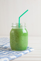Green smoothie in a jar on a white wooden table.