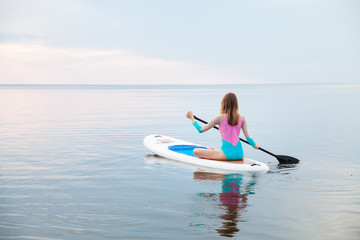 Unrecognizable young woman paddling on sup board