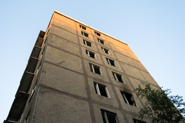 Corner of an abandoned multistory building. Broken windows, wood. Outdoor, sky. Urban.
