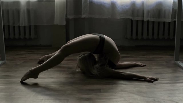 Young professional pole dancer shows gymnastic elements.
