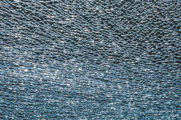 Texture of broken safety glass with sunbeams, in the dark background