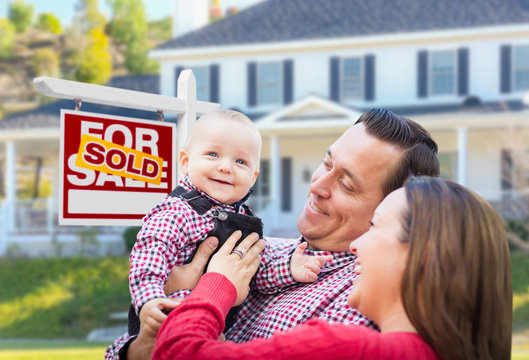 Happy Young Family In Front of Sold For Sale Real Estate Sign and House.
