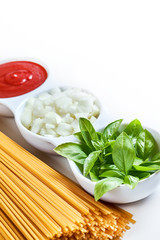 Basil, sliced onions and tomato paste in white bowl with raw spaghetti on white background. copy space