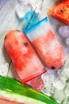 Frozen watermelon popsicles with ice cubes and watermelon slices on grey wooden background. Concept image for summer refreshments