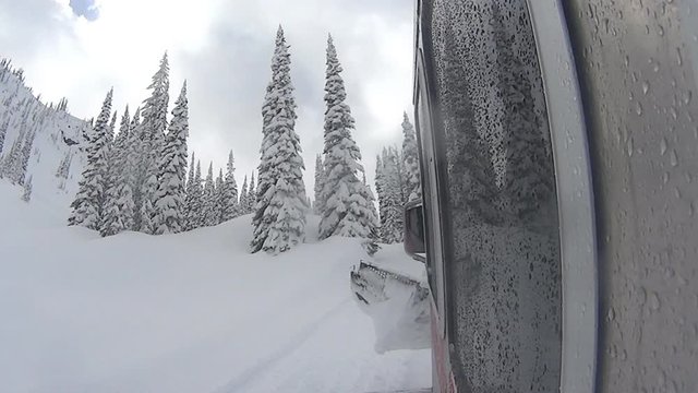 View of mountain peaks and an iced lake covered in deep snow, while ascending with a snow cat during a day of cat skiing. Location: Nelson, BC.
