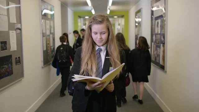  Portrait of young girl looking at book in busy school corridor
