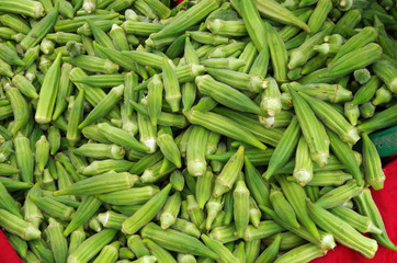 Bright green finger okra pouring from bucket onto red cloth display