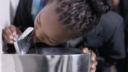  Young girl takes a drink from water fountain in school corridor.