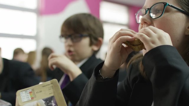  Happy young school children eating packed lunches in school cafeteria