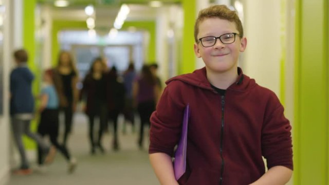  Portrait of young boy holding a folder in busy school corridor. 